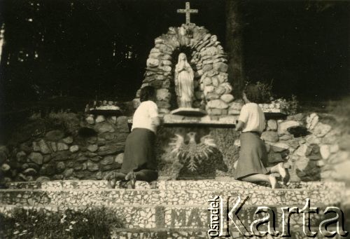 Sierpień 1943, Rumunia.
Dwie kobiety modlące się przy figurze Matki Boskiej ustawionej w kamiennej kapliczce, pod figurą ułożony z kamieni Biały Orzeł, na prowadzących do kapliczki schodach data: 