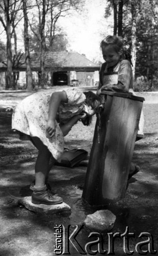 ok. 1950, Śląsk, Polska.
Dwie dziewczynki stojące przy studni, jedna z nich pije wodę, z tyłu leży szkolny tornister.
Fot. Kazimierz Seko, zbiory Ośrodka KARTA
