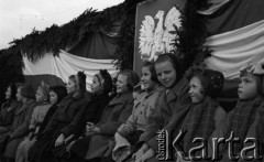 ok. 1950, Śląsk, Polska. 
Uroczystości państwowe, grupa dzieci siedzących przed trybuną honorową udekorowaną gałązkami świerku, biało-czerwoną flagą oraz polskim godłem.
Fot. Kazimierz Seko, zbiory Ośrodka KARTA