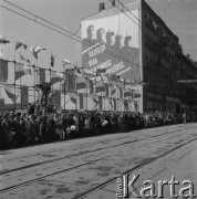 1.05.1972, Katowice, Polska.
Ludzie stojący wzdłuż ulicy w oczekiwaniu na przejście pochodu pierwszomajowego, z lewej na podwyższeniu kamera TVP, na ścianie budynku wisi plakat przedstawiający robotników z hasłem: 