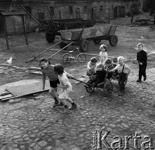 Maj 1970, Polska
 Dzieci bawiące się na podwórku, w tle rowerek i dwie furmanki.
 Fot. Jarosław Tarań, zbiory Ośrodka KARTA [70-30]
   
