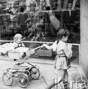 Sierpień 1970, Warszawa, Polska.
 Dziewczynka z młodszą siostrzyczką w wózku, w tle witryna sklepu.
 Fot. Jarosław Tarań, zbiory Ośrodka KARTA [70-126]
   
