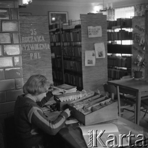 Maj 1979, Nasielsk, woj. ciechanowskie, Polska.
Wnętrze czytelni. Bibliotekarka sprawdza sygnatury książek w katalogu kartkowym. Na drugim planie widoczne są regały z książkami oraz napis: 