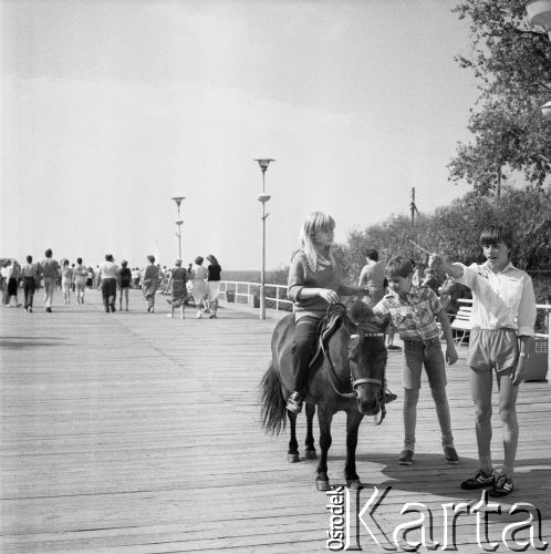 Lipiec 1986, Międzyzdroje, Polska 
Molo, dziewcznka siedząca na kucyku, obok stoją dwaj chłopcy, w tle widać morze.
Fot. Jarosław Tarań, zbiory Ośrodka KARTA, [86-82]