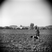Wrzesień 1968, Polska
W drodze na polowanie - myśliwy ze strzelbą oraz towarzyszącym mu psem przemierzają pola uprawne, w oddali - wiejska zabudowa, stogi siana, lasy.  
Fot. Jarosław Tarań, zbiory Ośrodka KARTA