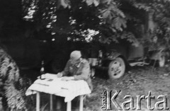 1941-1941, prawdopodobnie ZSRR. 
Żołnierz Wehrmachtu siedzący przy stoliku, z tyłu zamaskowane samochody.
Fot. NN, zbiory Ośrodka KARTA, zdjęcia z kolekcji Herberta Joosta udostępnił Krzysztof Kuczyński.

