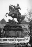 Koniec lat 80., Gdańsk, Polska.
Manifestacja gdyńskiej Federacji Młodzieży Walczącej pod pomnikiem króla Jana III Sobieskiego. Przed pomnikiem stoją mężczyźni z transparentem: 