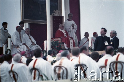 10.06.1987, Tarnów, Polska.
Trzecia pielgrzymka papieża Jana Pawła II do Polski w dniach 8-14 czerwca 1987 roku. Msza święta sprawowana przez Ojca Świętego, podczas której papież beatyfikował Karolinę Kózkównę. Z lewej siedzą arcybiskup metropolita krakowski kardynał Franciszek Macharski i biskup tarnowski Jerzy Ablewicz, obok Jana Pawła II stoi ksiądz Piero Marini, Mistrz Papieskich Ceremonii Liturgicznych, poniżej prymas Polski kardynał Józef Glemp.
Fot. Edward Grochowicz, zbiory Ośrodka KARTA