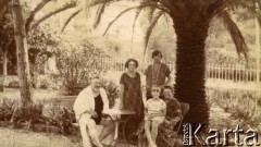1925-1927, Juan-les-Pins, Francja.
Grupa osób siedząca przy stoliku w ogrodzie. Z lewej redaktor Bogusławskij, z prawej Larysa Zajączkowska na kolanach u babci Larysy Michelson. Za nimi stoi Larissa Winterfeld, właścicielka pensjonatów 