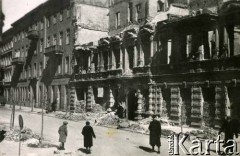 Od sierpnia 1940, Warszawa, Generalne Gubernatorstwo.
Przechodnie na ulicy, w tle widoczna kamienica, uszkodzona podczas bombardowań lotnictwa niemieckiego we wrześniu 1939 roku.
Fot. Larysa Zajączkowska, zbiory Ośrodka KARTA