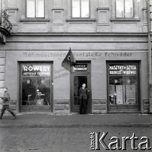 Wiosna 1940, Rzeszów, dystrykt krakowski, Generalne Gubernatorstwo.
Zakład Mechaniczny Franz Kaniewski - rowery, artykuły sportowe, maszyny do szycia - szyldy w języku niemieckim i polskim, przy Lorenzstrasse 15 (nazwa za czasów okupacji niemieckiej, obecnie ul. Grunwaldzka 24). Po lewej przechodzi żołnierz niemiecki.
Fot. NN, kolekcja Bogusława Kotuli, zbiory Fundacji Ośrodka KARTA
